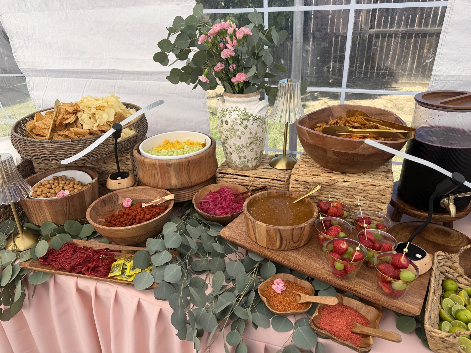 Bloom decorated snack table with chips, fruit cups, chamoy and agua de Jamaica